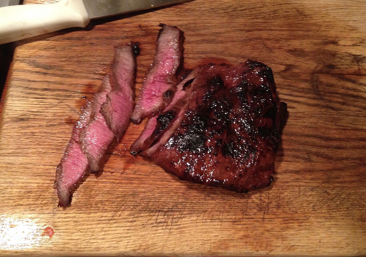 Sliced marinated steak with a browned crust on a wooden board
